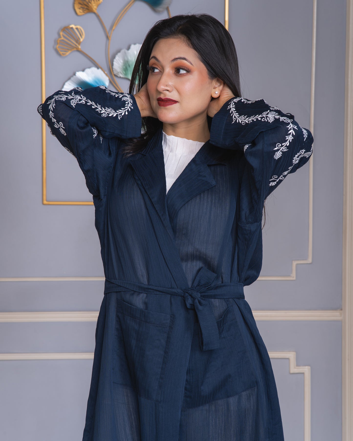 Woman wearing a navy blue outfit with white embroidery against a decorative wall.
