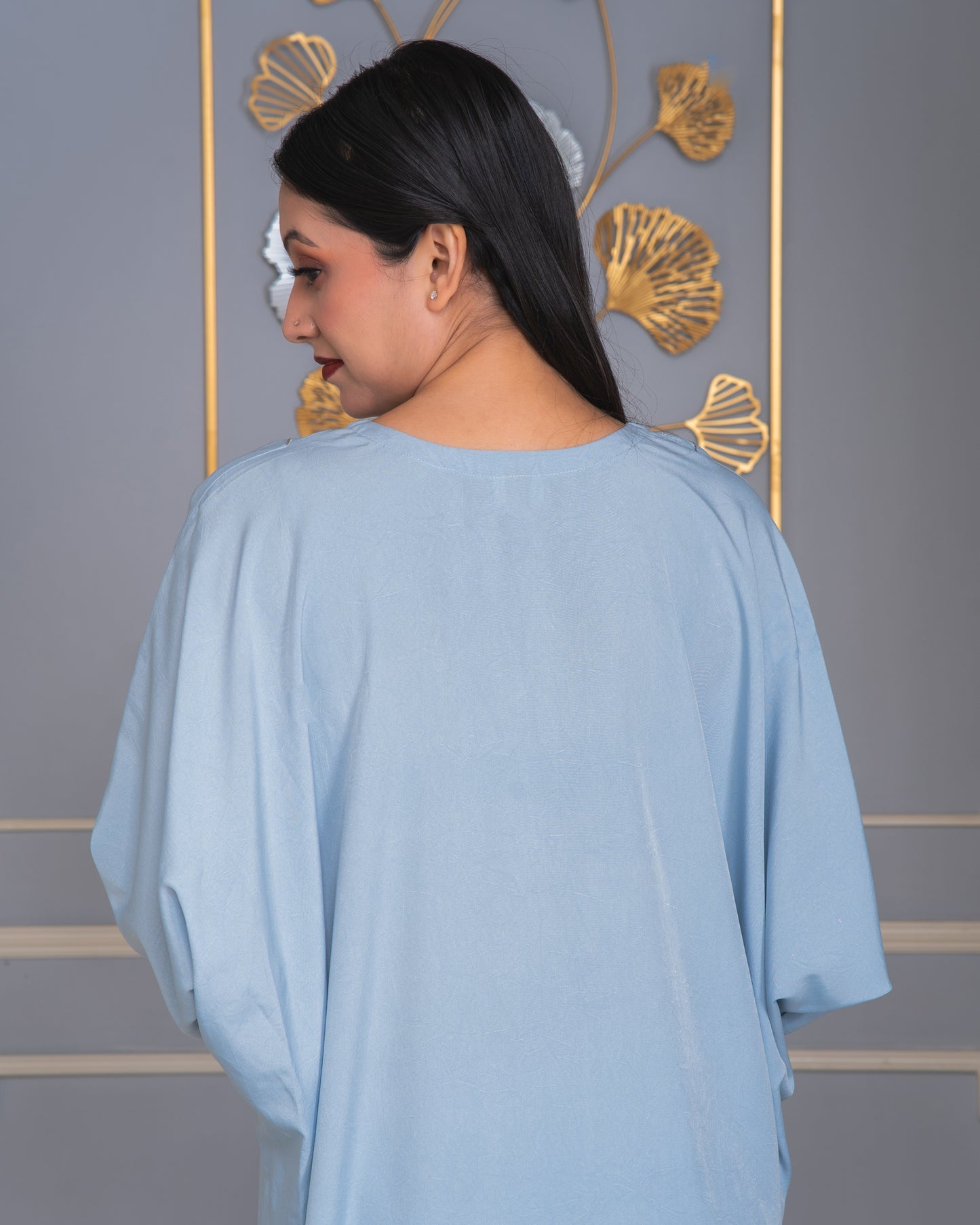 Woman wearing a light blue poncho against a decorative wall.