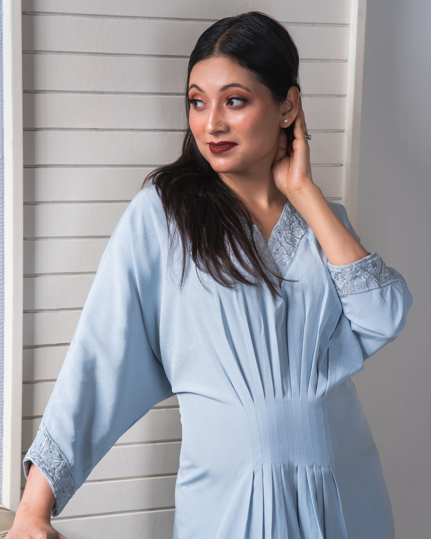 Woman wearing a light blue dress with lace details against a neutral background