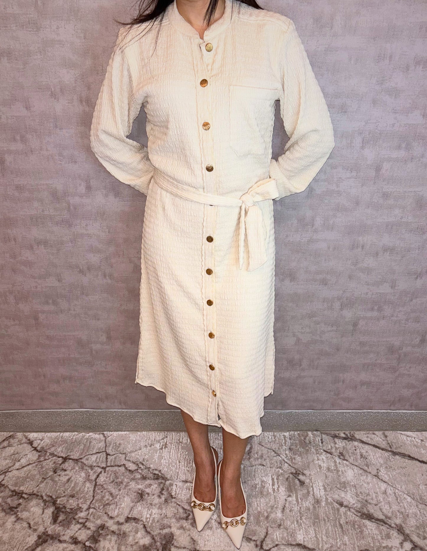 Experience versatile elegance with the Gilded Ivory Dress, a highlight of Taraashi's Platinum Collection. Crafted from uniquely textured fabric in ivory, this versatile piece blends everyday comfort with understated polish. Styled like a classic shirt dress with a defining tie belt, it's distinguished by a row of luminous gold buttons lending an elevated touch.