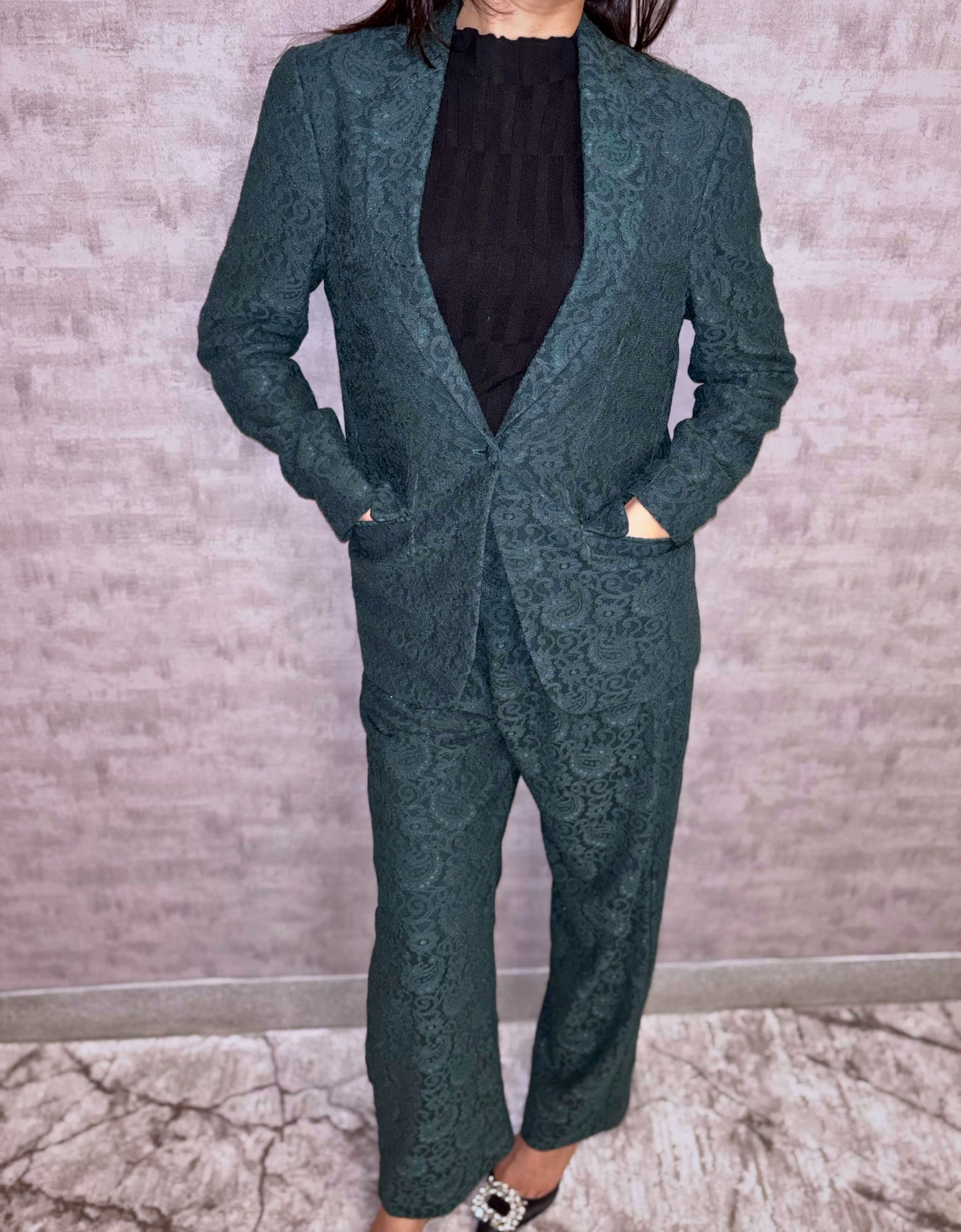Step into sophisticated elegance with this captivating deep green pantsuit. An intricate tapestry pattern graces the luxurious fabric, whispering quality while lending unique visual depth. The impeccably tailored silhouette balances modern structure with inherent feminine grace, designed to move fluidly with poise. This stunning ensemble speaks volumes of quiet confidence and undeniable allure.