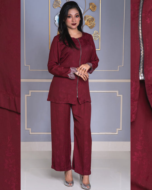 Woman wearing a burgundy outfit with floral embroidery against a decorative wall.