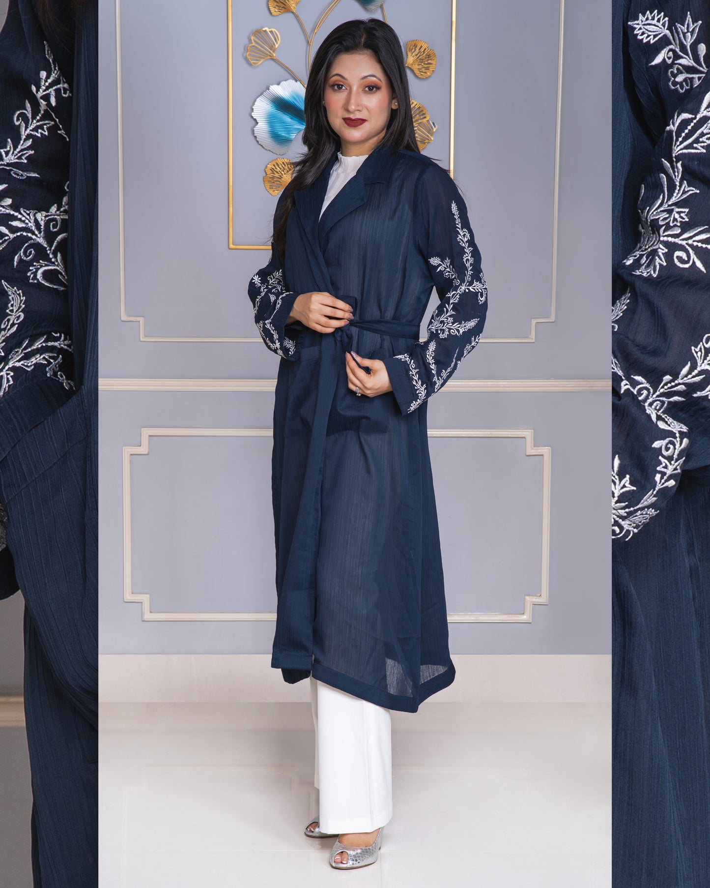 Woman wearing a navy blue embroidered abaya with white pants against a decorative wall.