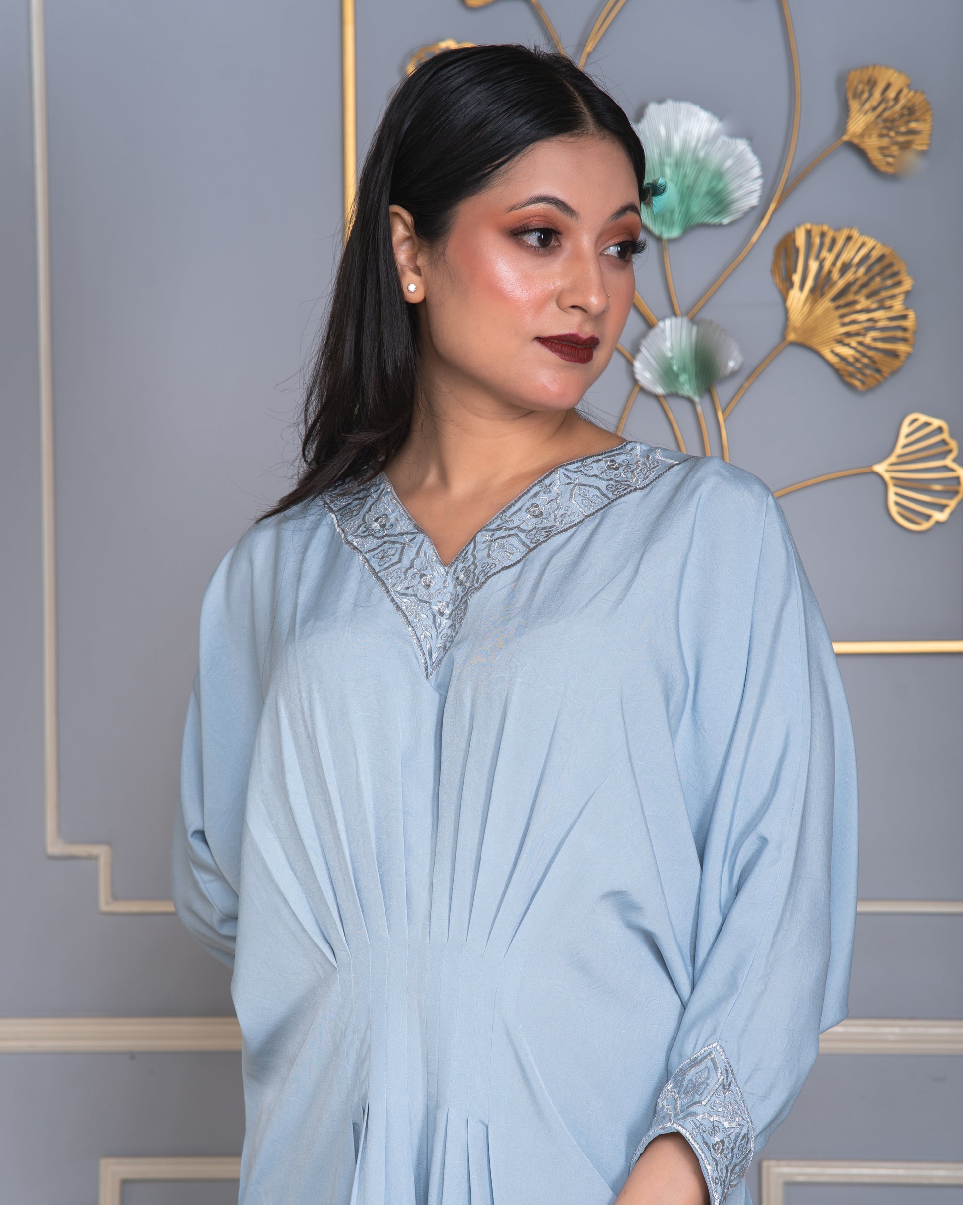 Woman wearing a light blue dress with lace details against a decorative wall.