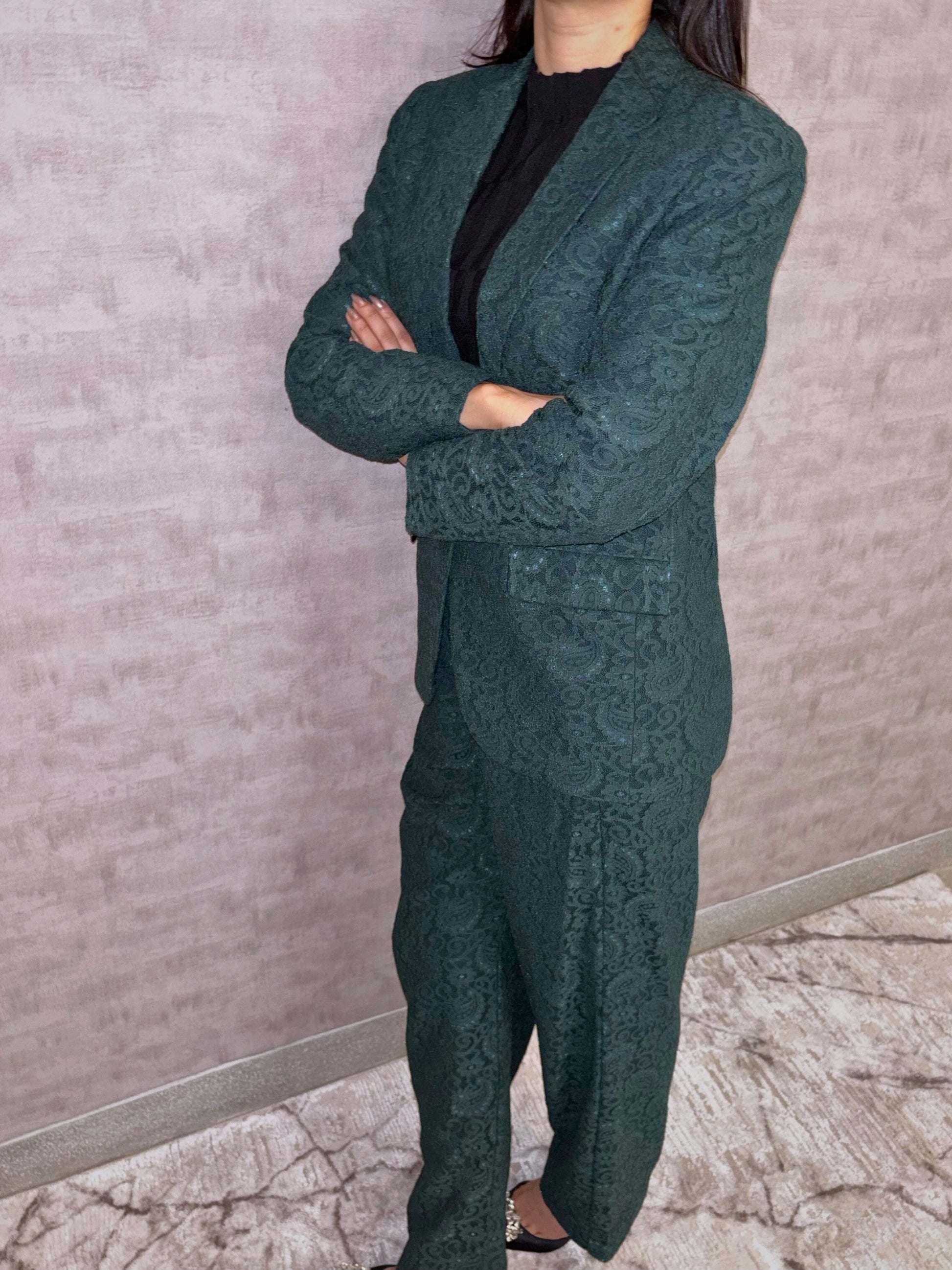 Step into sophisticated elegance with this captivating deep green pantsuit. An intricate tapestry pattern graces the luxurious fabric, whispering quality while lending unique visual depth. The impeccably tailored silhouette balances modern structure with inherent feminine grace, designed to move fluidly with poise. This stunning ensemble speaks volumes of quiet confidence and undeniable allure.