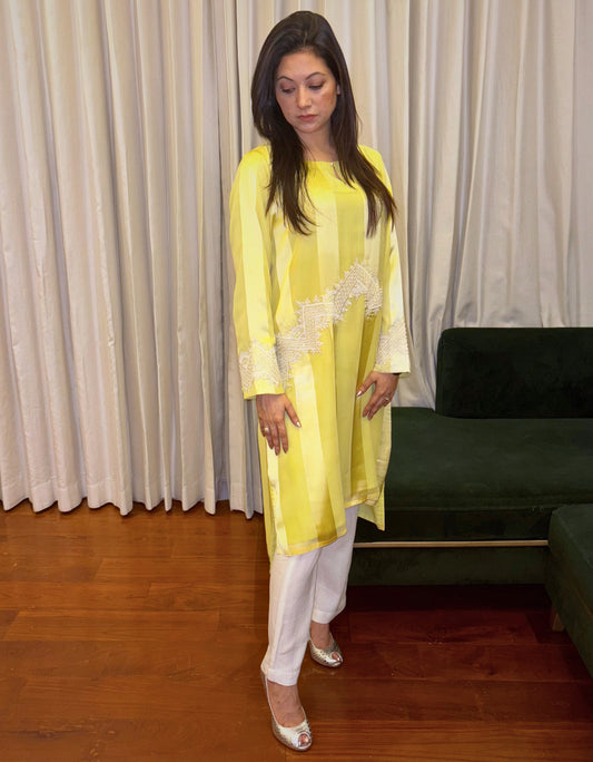 Elevate your wardrobe with the Citrus Beam Kurti Set, a lemon yellow kurti set designed for effortless sophistication. Crafted from lustrous striped fabric, this long kurti set features intricate ivory embroidery and handwork (Karchupi) across the waist and sleeves—balancing minimalism with detailed craftsmanship.

Ideal for festive gatherings or formal daytime occasions, this embroidered kurti set for women is a refreshing take on contemporary ethnic wear.