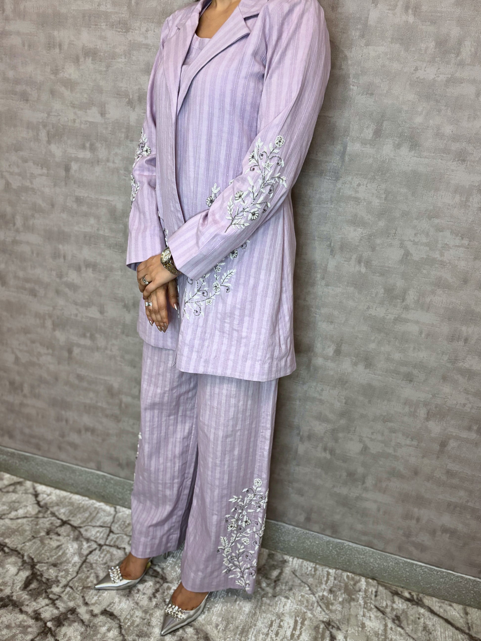 From Taraashi's exclusive Platinum Collection, this charming lilac ensemble offers sophisticated ease. Subtle stripes meet delicate silver or white embroidery gracing the flowing jacket and trousers. The three-piece set blends soft texture with intricate artistry for a light, airy feel. Experience effortless elegance and the refined quality unique to our Platinum pieces.