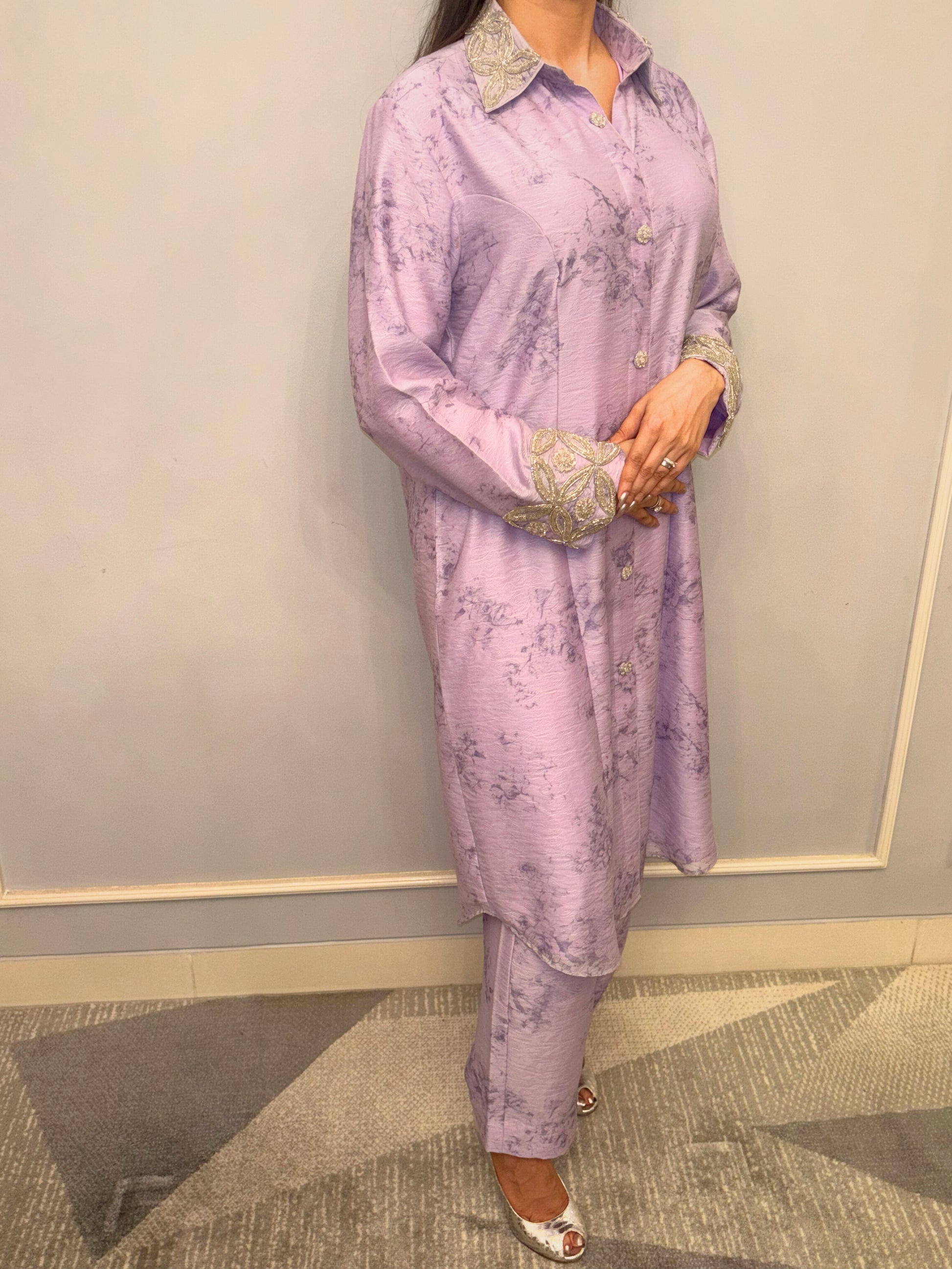 Bathed in the soft luminescence of a lilac dawn, this Taraashi Kurti Set exudes a quiet yet captivating sophistication. The flowing silhouette, adorned with delicate silver handwork (zardousi work) at the collar and cuffs, speaks of refined artistry.

The subtle texture of the fabric adds depth to the serene hue, creating an ensemble that is both graceful and contemporary. It's an expression of understated luxury, perfect for moments where poise and elegance take center stage.