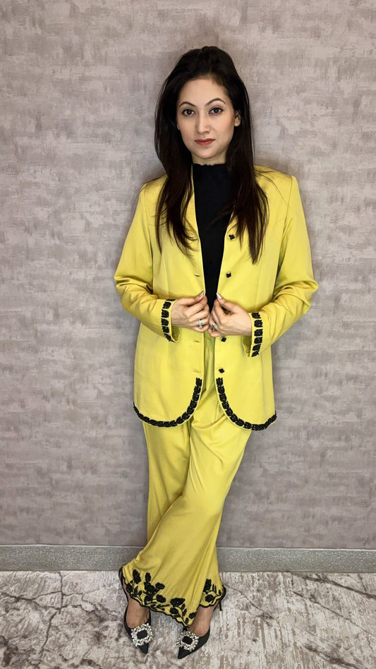 Ignite your presence with the captivating Golden Hour Ember Pantsuit. Luminous yellow fabric sets a vibrant stage for dramatic black embellishments that trace the cuffs and hems with intricate, ember-like artistry. The silhouette offers sharp tailoring, softened by the jacket's unique curved edges and the graceful flow of wide-leg trousers. This stunning ensemble radiates bold femininity and contemporary chic, ensuring you stand out with undeniable allure.